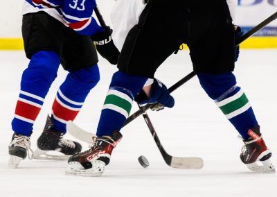 Two hockey players in action on the ice, focusing on their skates and sticks.