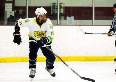 A hockey player in a white jersey and helmet is on the ice, with an official nearby.