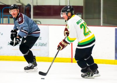 Two hockey players on the ice, one in a white jersey, the other in blue, competing for the puck.