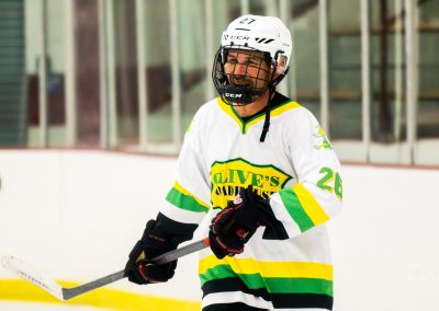 A hockey player in a white and green jersey with the number 26 is skating on the ice.